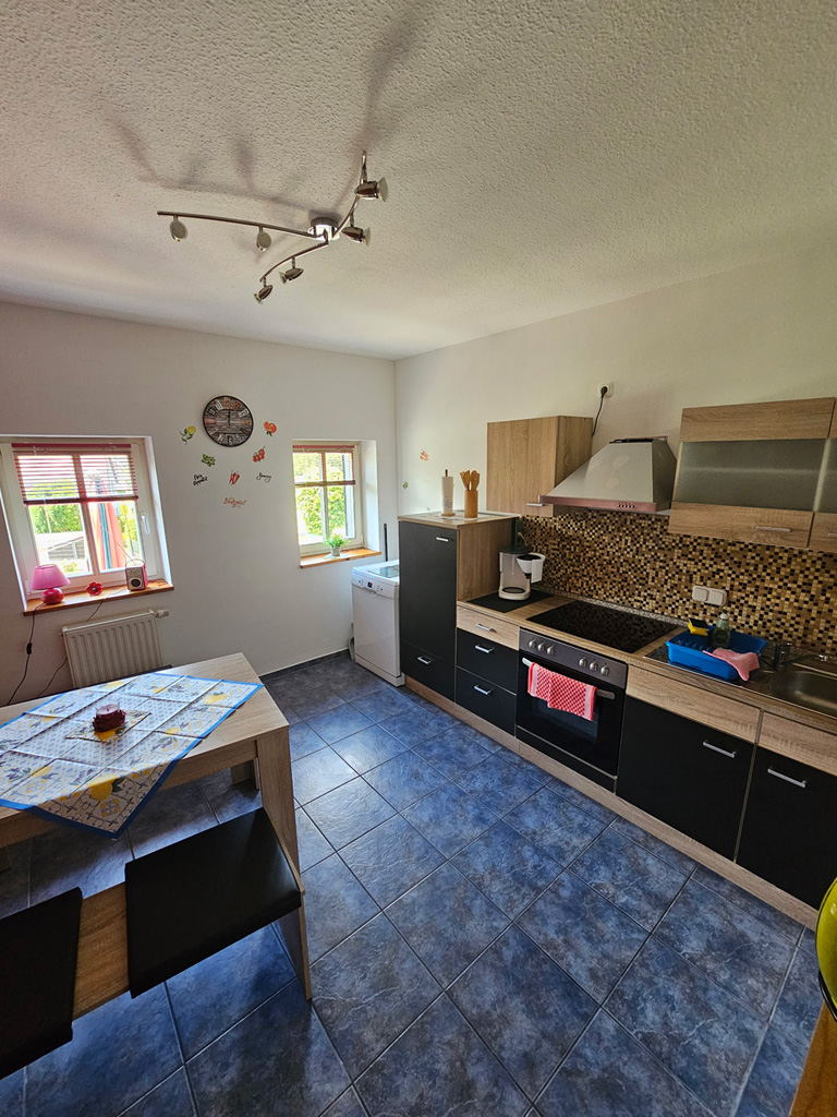 Küche einer Ferienwohnung mit Essplatz, Herd und Fenster zum Grün