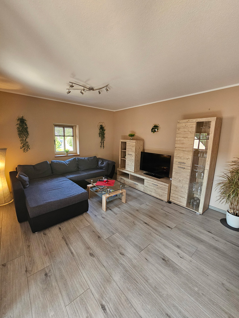 Heller Wohnraum einer Ferienwohnung mit großer Eckcouch, Sideboard und Dielenboden