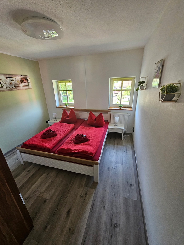 Schlafzimmer einer Ferienwohnung mit Doppelbett und roter Bettwäsche