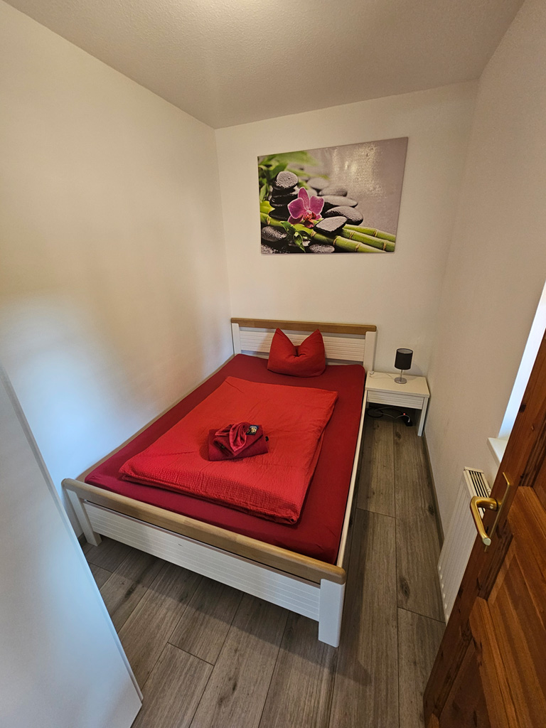 Kleines Schlafzimmer mit Einzelbett und roter Tagesdecke